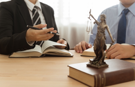 Two men in suits with a law book and lady justice